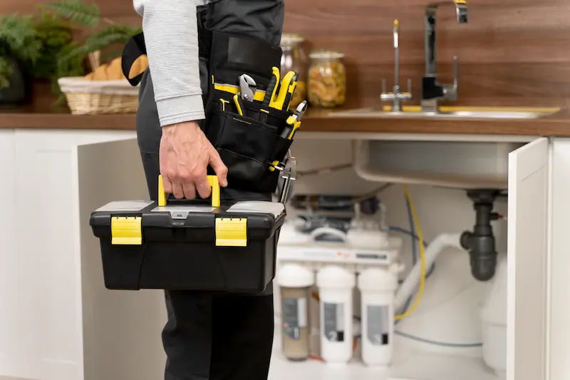 Plombier arrivant avec sa caisse à outils devant un évier